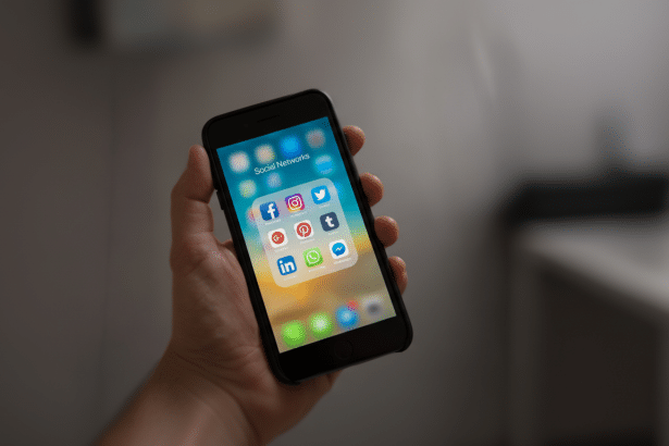 A hand holding a smartphone displaying a folder of social network applications like Facebook, Instagram, Twitter, and more, resized to a 1 6: 9 aspect