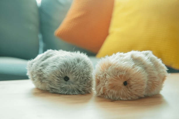 Two furry , robotic pets, one gray and one light brown , resting on a wooden table with soft focus pillows in the background.