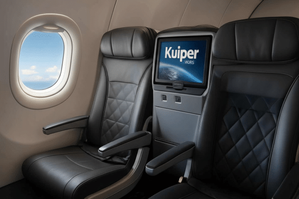 An interior view of an airplane cabin showing two rows of black leather seats and a window with a blue sky visible outside . One seatback features an entertainment screen displaying the Kuiper by V ias at logo.