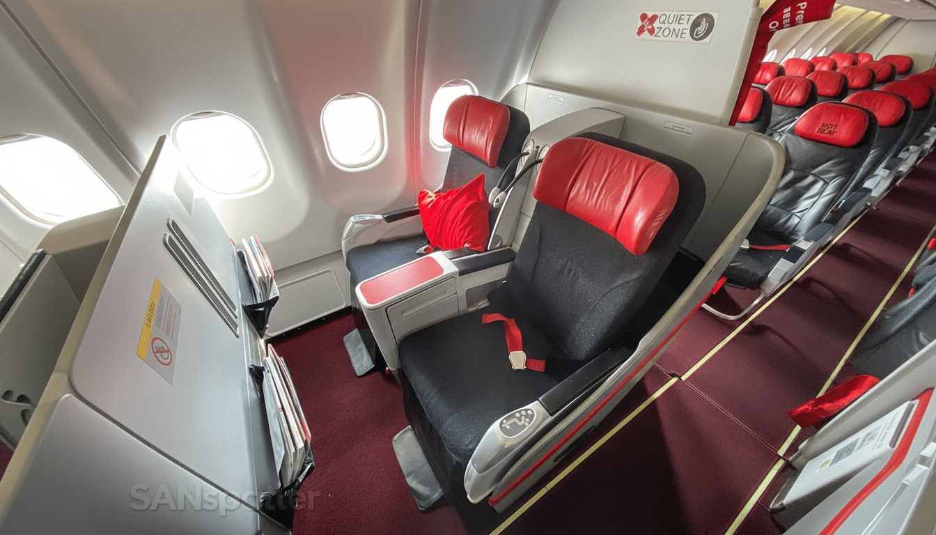 Interior view of an airplane cabin showing rows of seats, with red and black upholstery, near windows. A Quiet Zone sign is visible.