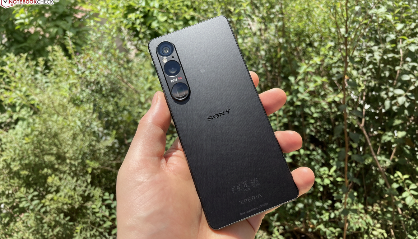 A hand holding a black Sony Xperia smartphone, showcasing its rear camera setup and textured back, against a blurred green foliage background.