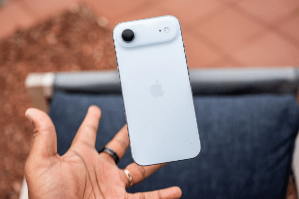 A hand holding a white iPhone with a single camera lens and Apple logo on the back, presented in a 16: 9 aspect ratio with the original background ret