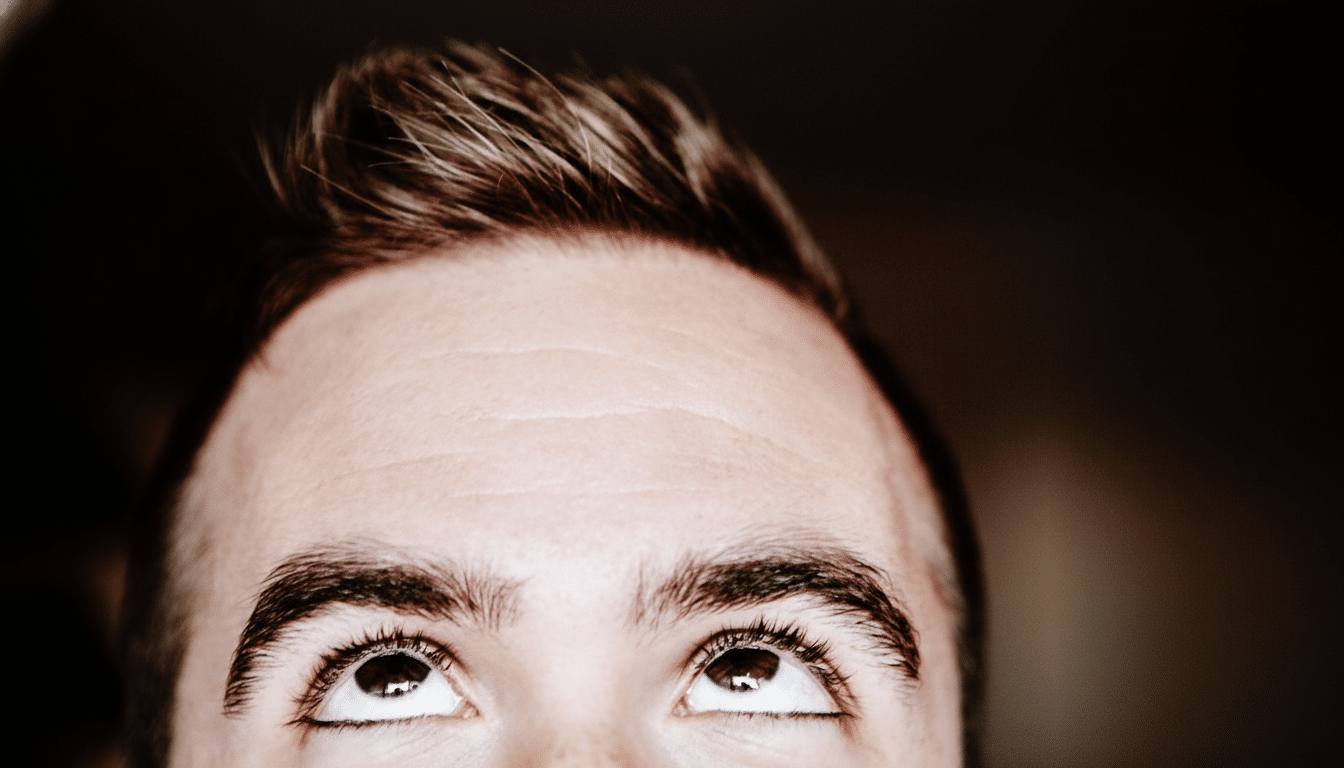Close- up of a man 's forehead and eyes looking upwards with a dark background.