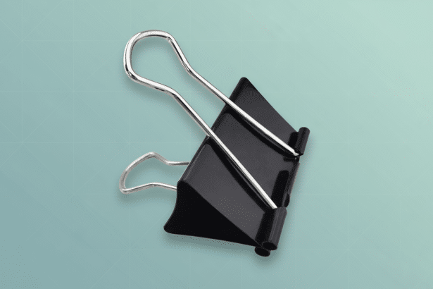 A black binder clip with silver handles on a light blue background with a subtle geometric pattern .