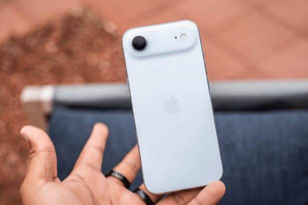 A hand holding an iPhone SE (20 22) in white, showcasing its back camera and Apple logo.