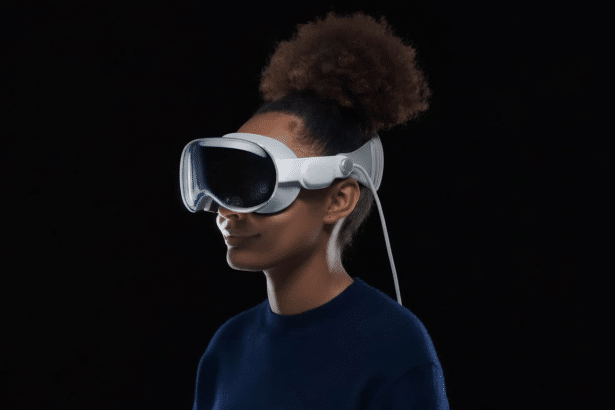 A person with dark, curly hair in a bun wearing a white virtual reality headset against a dark background, looking slightly to the right. Filename : personvr headset blackbackground. png