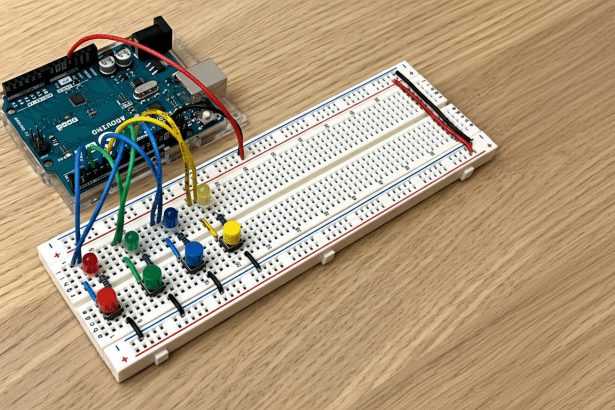 An Arduino board connected to a bread board with LEDs and buttons on a wooden surface.