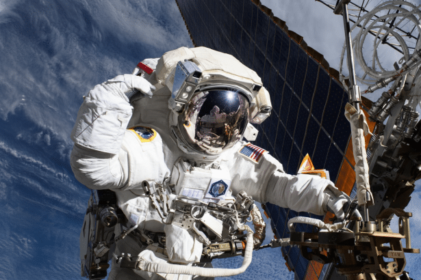 An astronaut in a white spaces uit is depicted against the backdrop of Earth and a solar panel, working on external equipment. Filename : astronautworking on equipment .png