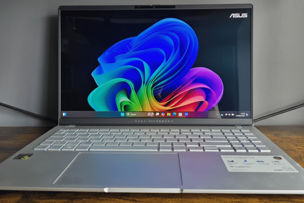A professional shot of an ASUS Vivobook S 15 laptop with a colorful abstract wallpaper on its screen, set on a wooden surface against a gray background. Filename : asus vivobook s1 5laptop .png