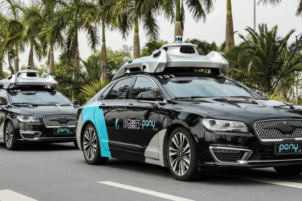 Three black autonomous Pony.ai cars with blue accents drive in a line on a road lined with palm trees.