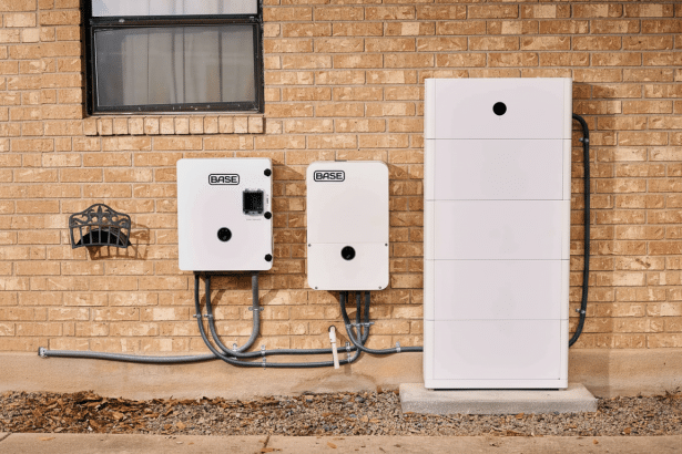 Three white BASE brand energy units and a battery storage system mounted on a brick wall .