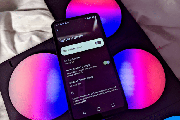 A smartphone displaying the Battery Saver settings in a dark theme , with the Use Battery Saver toggle set to off . The phone is placed on a surface with colorful, illuminated circular objects in the background.