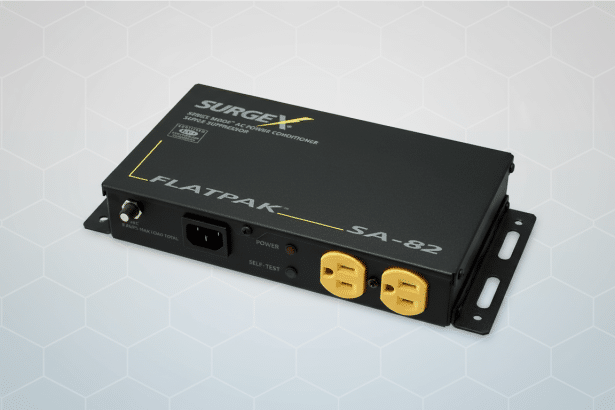 A black SurgeX Flatpak SA-82 AC power conditioner with two yellow outlets , against a professional flat gray background with a subtle hexagonal pattern.