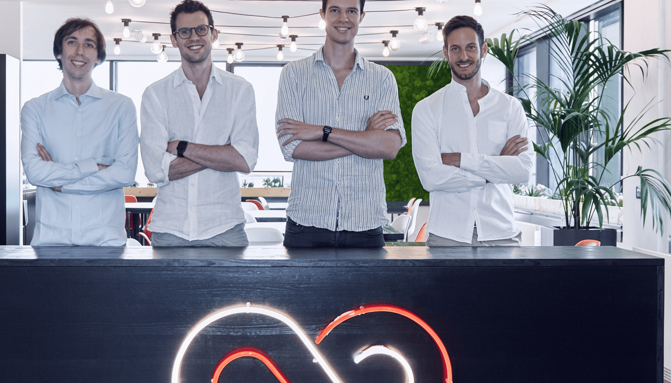 Four men standing behind a counter with a neon logo, resized to a 1 6: 9 aspect ratio.