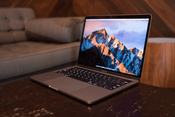 A professional shot of a MacBook Pro with a mountain landscape on its screen, placed on a dark wooden table. The background features a blurred, modern