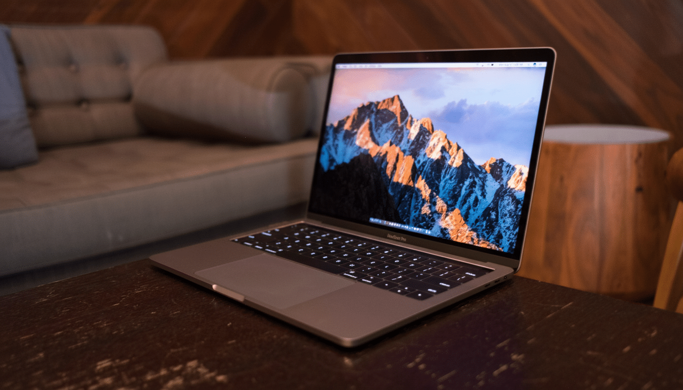 A professional shot of a MacBook Pro with a mountain landscape on its screen, placed on a dark wooden table. The background features a blurred, modern