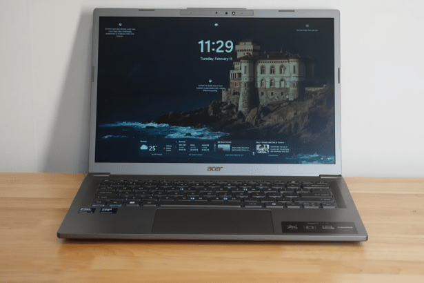 A professional shot of a silver Acer laptop with a dark lock screen displaying the time, date, weather, and a castle by the sea.