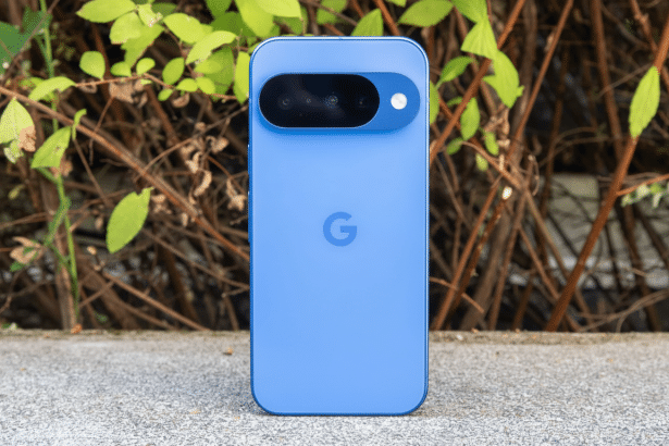 Blue Google Pixel phone with a black camera bar, resting on a concrete surface with green leaves and brown branches in the background.