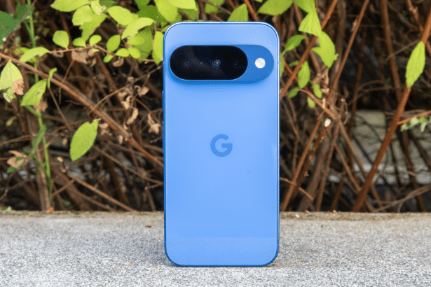 A blue Google Pixel smartphone displayed vertically on a concrete surface with a natural background of green leaves and brown branches.