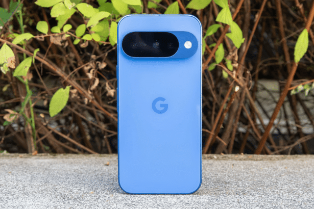A blue Google Pixel smartphone is centered on a concrete ledge , with green leaves and brown branches in the blurred background. The phone' s camera bar is visible at the top.