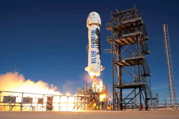 Blue Origin rocket launching from a desert launchpad with flames visible at the base , set against a clear blue sky. Filename : blueorigin rocketlaunch .png