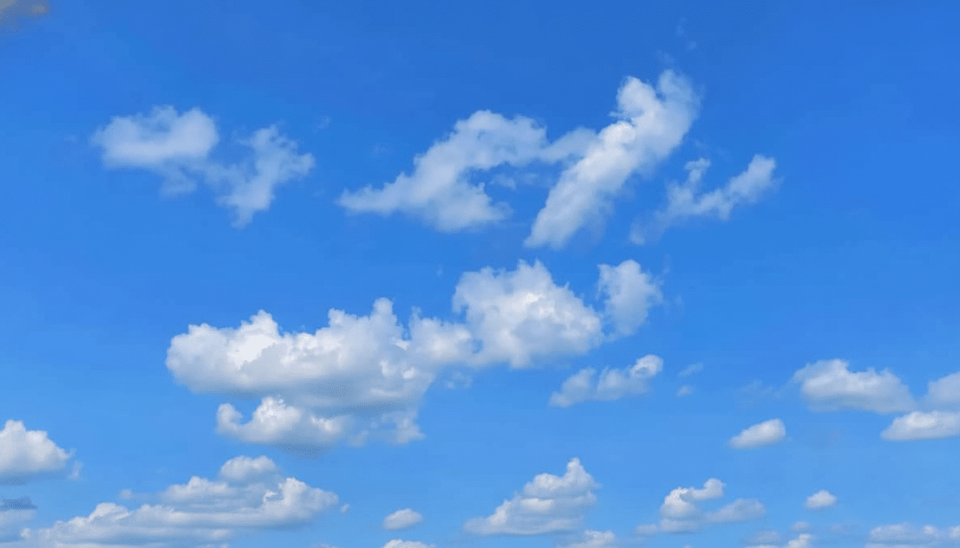 A bright blue sky with scattered white cumulus clouds.