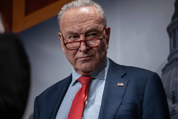 Chuck Schumer in a suit and tie looking serious with his glasses lowered .