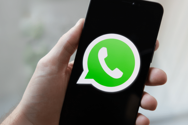 A hand holding a smartphone displaying the WhatsApp logo on a black screen , resized to a 16:9 aspect ratio.