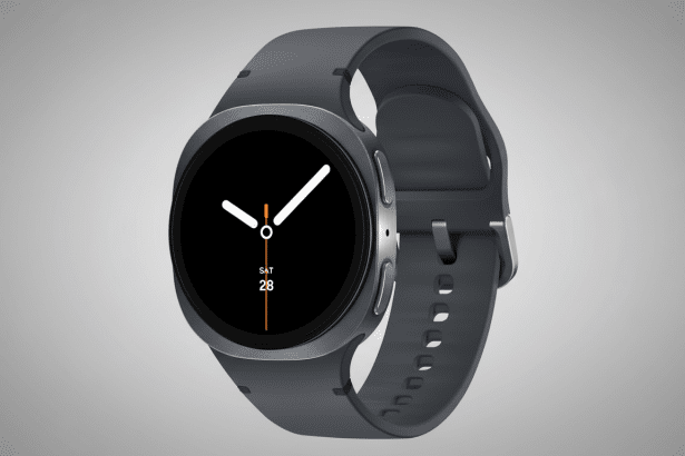 A professional shot of a dark gray smartwatch with a black circular display showing the time and date ( SAT 28 ). The watch has a silicone band and a brushed metal casing . The background is a soft gray gradient .