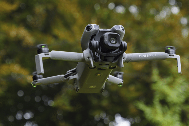 A DJI Mini 5 Pro drone hovering in mid -air against a blurred green foliage background.