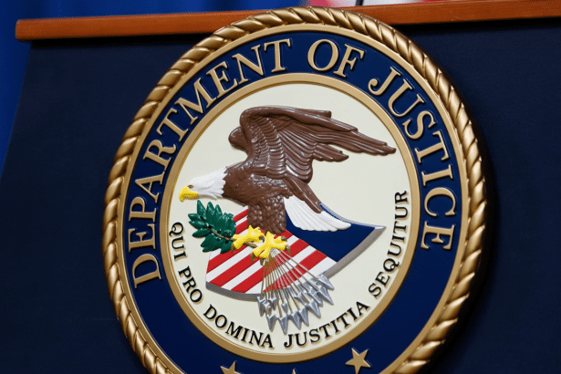 A professional , enhanced image of the Department of Justice seal, resized to a 1 6:9 aspect ratio, displayed on a dark blue podium . The seal features an eagle with an olive branch and arrows, encircled by the text DEPARTMENT OF JUSTICE and QUI PRO DOMINA JUST ITIA SE QUITUR.