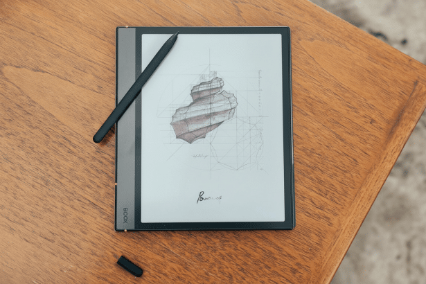 An e -reader with a stylus displaying a technical drawing of a spiral object, resting on a wooden table.