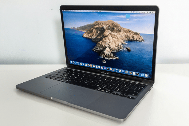 A professional shot of a silver MacBook Pro with its screen displaying a scenic island landscape , set against a plain white background.