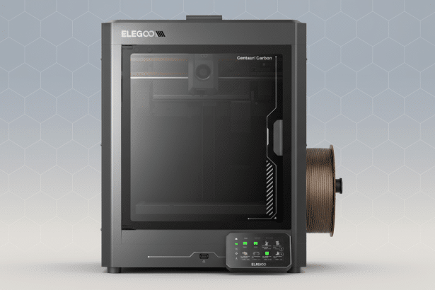 alt = An ELEGOO Centauri Carbon 3D printer, dark gray with a clear front panel, is centered on a li