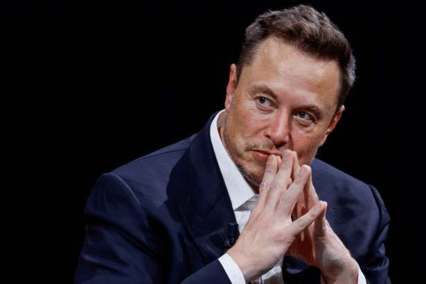 Elon Musk in a dark suit , looking intently to the left with his hands clasped under his chin.