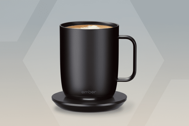 A sleek , black Ember smart mug with a latte art design on top, sitting on its charging coaster. The background is a professional flat design with soft gray and white geometric patterns. Filename : embersmart mugprofessional display .png