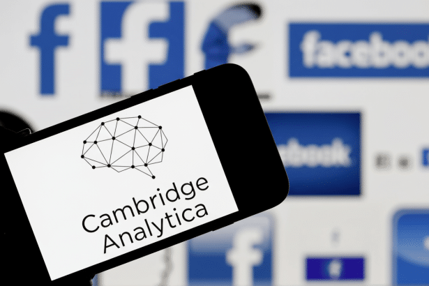 The Cambridge Analytica logo is displayed on a smartphone screen, with blurred Facebook logos in the