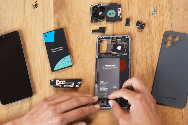 An overhead shot of a person's hands assembling a Fair phone on a wooden table , with various phone components laid out.