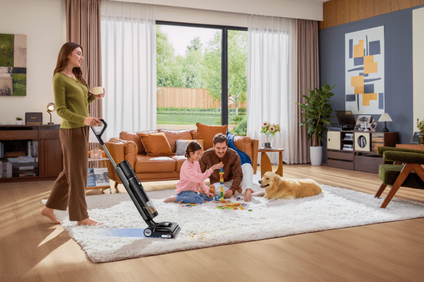 A family in a living room, with a woman using a vacuum cleaner, and a man and child playing on a rug with a golden retriever nearby .