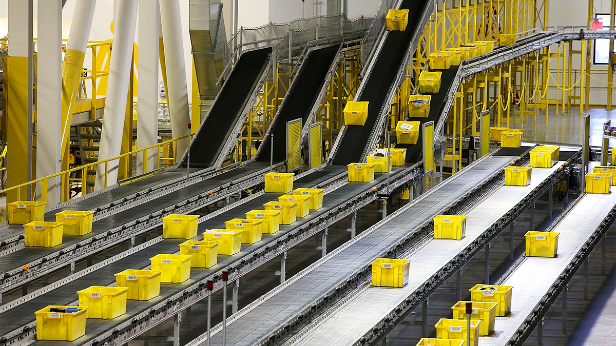 Robotic arms sorting packages on an Amazon warehouse conveyor belt, illustrating automation