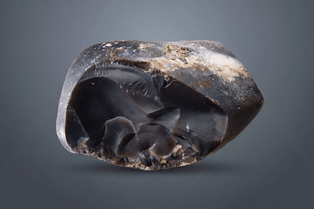 A dark, irregularly shaped flint stone with sharp edges and rough patches , centrally placed on a flat dark gray background with subtle geometric patterns.