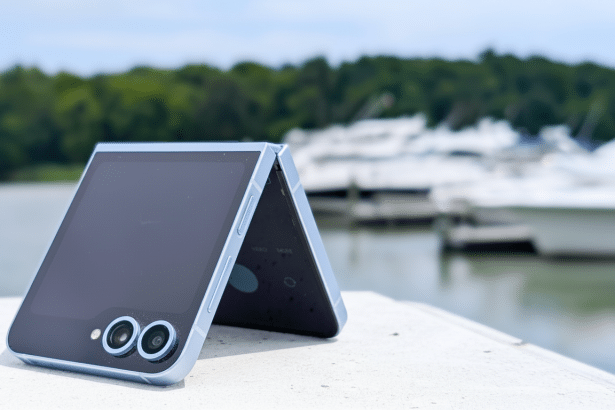 A light blue foldable smartphone with its screen partially open, resting on a white surface with a blurred background of boats in a harbor.