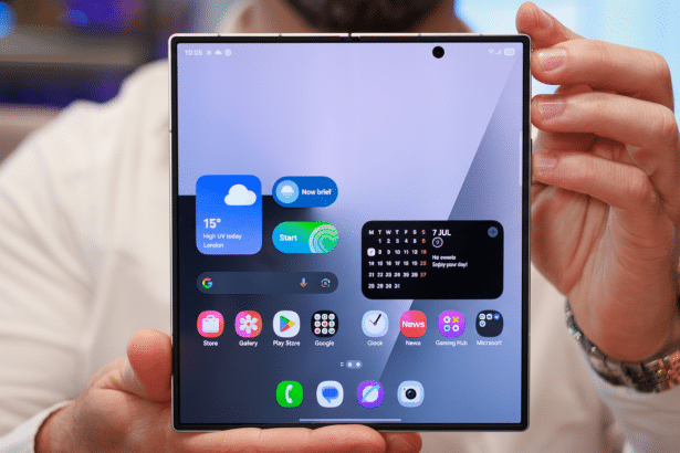 A person holding a foldable smartphone with its screen displaying the home interface with app icons and widgets.