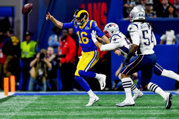 An American football player in a blue and yellow uniform, number 1 6, ev ades a tackle from a player in a white uniform, while another player in white