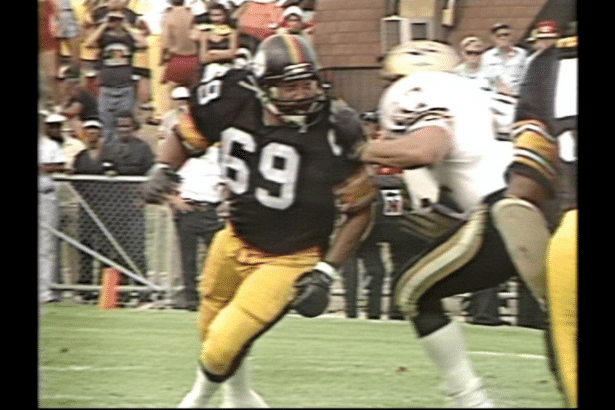 A professional football player wearing a black jersey with the number 69 and yellow pants, running on a green field during a game.