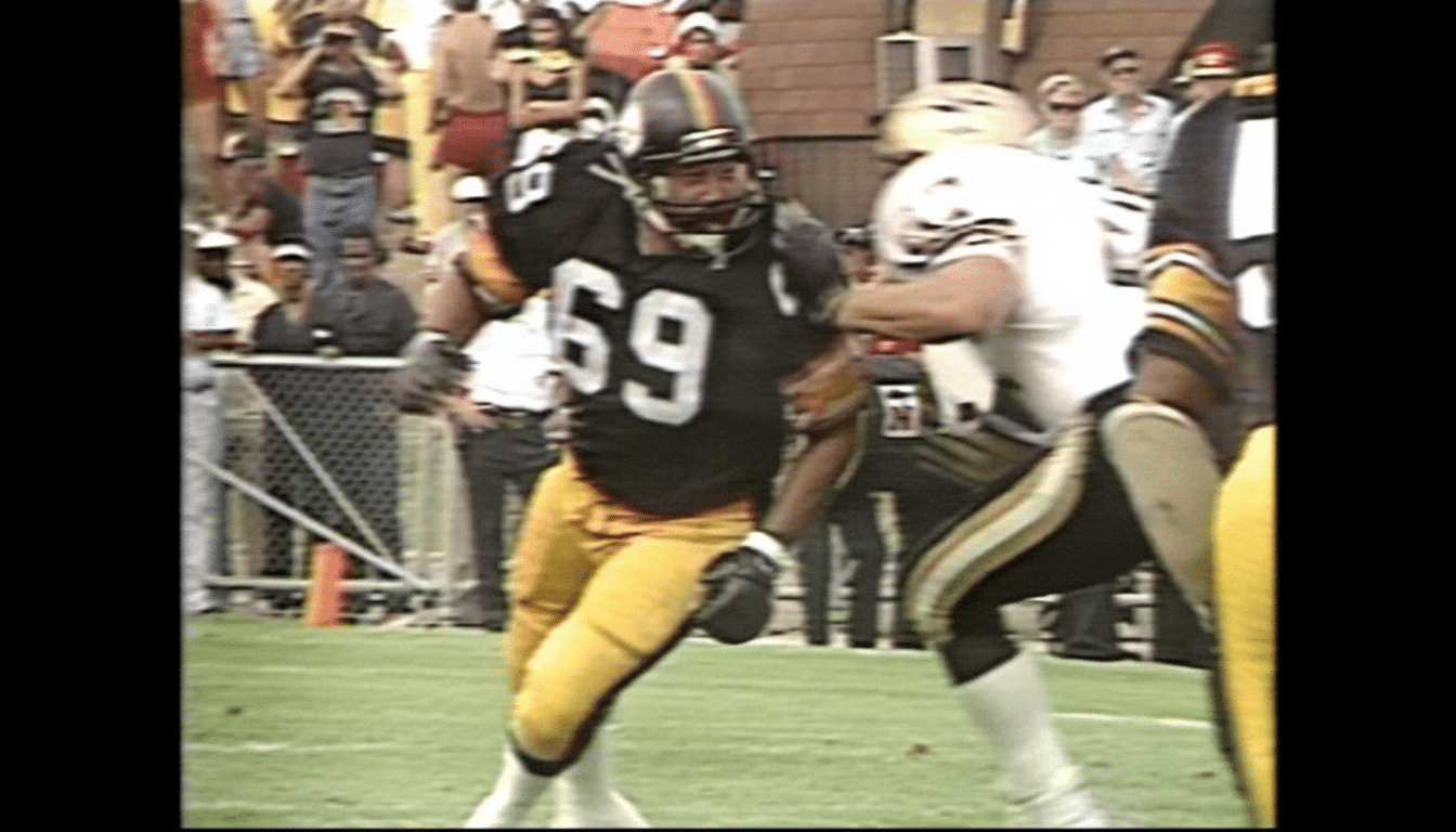 A professional football player wearing a black jersey with the number 69 and yellow pants, running on a green field during a game.