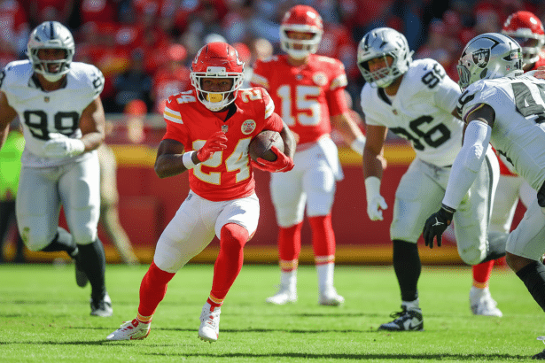 A professional American football player in a red jersey with the number 2 4, running with the ball on a green field during a game.