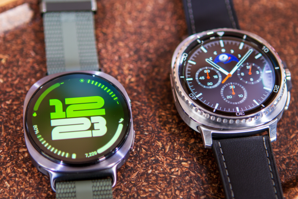 Two smartwatches, one with a digital display showing time and steps , and another with an analog chronograph face, resting on a textured brown surface. Filename : smart watches16 9. png