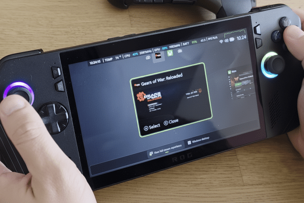 Hands holding a black gaming handheld with a screen displaying Gears of War: Reload ed. Filename : gaminghand heldge arsof war.png