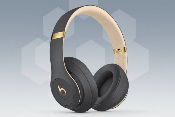A pair of Beats Studio3 Wireless headphones in matte gray with gold accents, presented professionally on a gray background with subtle hexagonal patte